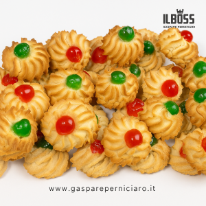 Dettaglio ravvicinato dei Ricci di Mandorla Siciliana con mandorle tostate e ciliegie candite, evidenziando la consistenza dorata e la texture artigianale del dolce su fondo bianco pulito.